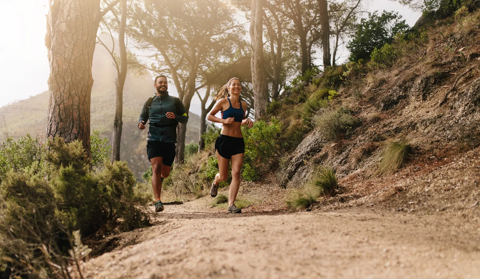 Un couple court sur un sentier forestier de montagne, illustrant une vie active et le retour au mouvement.